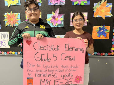 Two elementary students stand holding a poster about the Cereal Drive