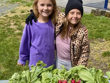 Two elementary female students stand in front of fresh radishes from the garden