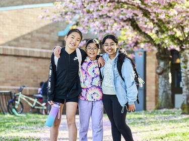 3 female elementary students in Abbotsford, BC underneath blossoming cherry trees