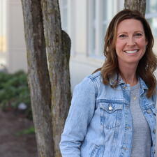 Female with short brown hair stands outside next to tree and smiles for photo